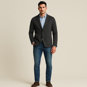 Man wearing a dark blazer, light blue shirt, and jeans on a beige background